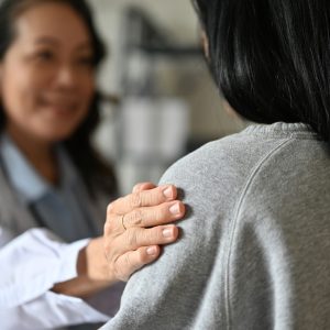 An aged Asian female doctor touching shoulder to comfort and support her patient. An aged Asian female doctor touching shoulder to comfort and support her patient. A young Asian female patient is being reassured by her doctor. close-up image